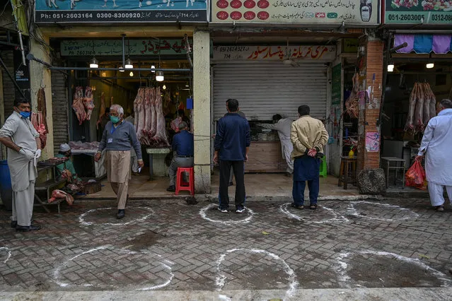 Customers stand in designated areas marked on the floor outside meat and grocery shops to maintain recommended social distancing during a government-imposed nationwide lockdown as a preventive measure against the COVID-19 coronavirus in Islamabad on March 26, 2020. (Photo by Aamir Qureshi/AFP Photo)