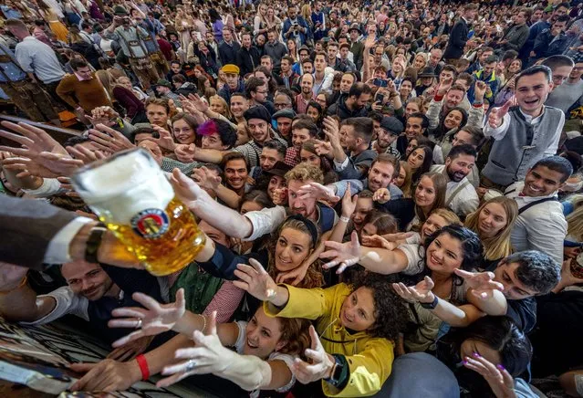 Young people reach out for free beer in one of the beer tents on the opening day of the 187th Oktoberfest beer festival in Munich, Germany, Saturday, September 17, 2022. Oktoberfest is back in Germany after two years of pandemic cancellations, the same bicep-challenging beer mugs, fat-dripping pork knuckles, pretzels the size of dinner plates, men in leather shorts and women in cleavage-baring traditional dresses. (Photo by Michael Probst/AP Photo)