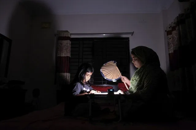 A Bangladeshi woman uses a traditional hand fan as she assists her daughter in her studies during a power cut at their home in Pilkhana area, Dhaka, Bangladesh, Tuesday, August 23, 2022. Schools in Bangladesh will close an additional day each week and government offices and banks will shorten their work days by an hour to reduce electricity usage amid concerns over rising fuel prices and the impact of the Ukraine war. (Photo by Mahmud Hossain Opu/AP Photo)