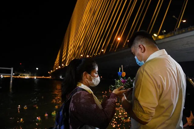 A couple holds a Krathong or “floating basket” near Chao Phraya river amid a yearly festival during which rafts of neatly folded banana leaves, decorated with flowers, candles and incense, are offered to thank the water goddess for good luck and for using her water to grow crops and support all life in Bangkok, Thailand on November 8, 2022. (Photo by Chalinee Thirasupa/Reuters)