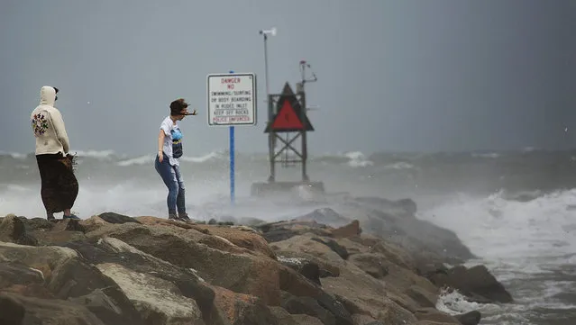 Near to a warning sign to keep off the rocks, people take photos along Rudee Inlet in Virginia Beach, Va. as the remnants of Hermine makes it way up the coast on Saturday, September 3, 2016. Forecasters said the system could strengthen back into a hurricane Monday through Wednesday as it moves on an offshore path from the waters of Maryland to Connecticut, before weakening again off New England. (Photo by L. Todd Spencer/The Virginian-Pilot via AP Photo)