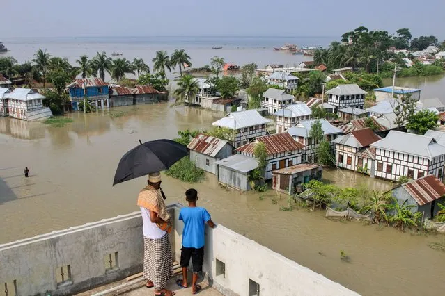 A man and a kid on a roof top look at the flood affected area in Munshiganj on August 3, 2020. One third of Bangladesh is under water after some of the heaviest rains in a decade leaving more than 3 million people affected with homes and roads in villages flooded, Flood Forecasting and Warning Centre (FFWC) officials said. (Photo by Sultan Mahmud Mukut/SOPA Images/LightRocket via Getty Images)