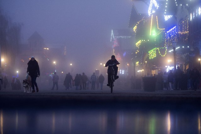 A person pedals a bike past storefronts decorated with Christmas lighting on Front Street, in Leavenworth, Wash., November 26, 2024. (Photo by Jenny Kane/AP Photo)