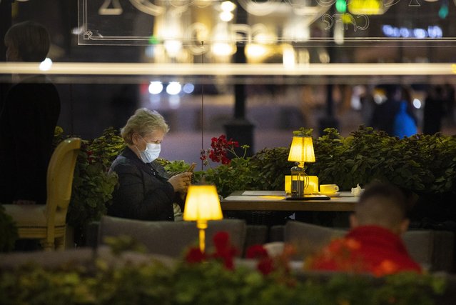 A woman, wearing a face mask to protect against coronavirus enjoys a warm evening sitting at a street-side cafe in the center of Moscow, Russia, Friday, September 25, 2020. Moscow authorities have issued a recommendation for the elderly to stay at home and for employers to allow as many people as possible to work remotely, following a rapid growth of the coronavirus caseload in the Russian capital. (Photo by Alexander Zemlianichenko/AP Photo)