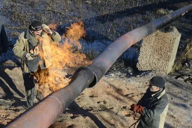 Workers repair a gas pipeline damaged during shelling between Ukrainian forces and pro-Russian militants in eastern Ukrainian village Krasnyi Pakhar, in the Donetsk region on November 23, 2014. (Photo by Alexander Khudoteply/AFP Photo)