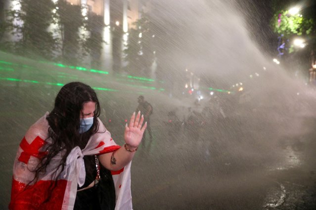 A woman reacts as law enforcement officers use a water cannon to disperse the crowd near the parliament building, during a rally to protest against a bill on “foreign agents” in Tbilisi, Georgia, on May 1, 2024. Georgian parliament is set to debate the second reading of the bill described as authoritarian and Russian-inspired by Georgia's opposition and Western countries. (Photo by Irakli Gedenidze/Reuters)