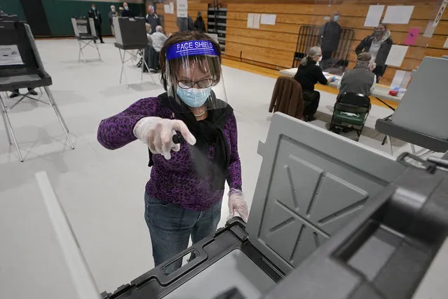 Poll worker Kathy Richardson uses a spray bottle to sanitize a voting booth out of concern for the coronavirus in a polling station at Marshfield High School, Tuesday, November 3, 2020, in Marshfield, Mass. (Photo by Steven Senne/AP Photo)