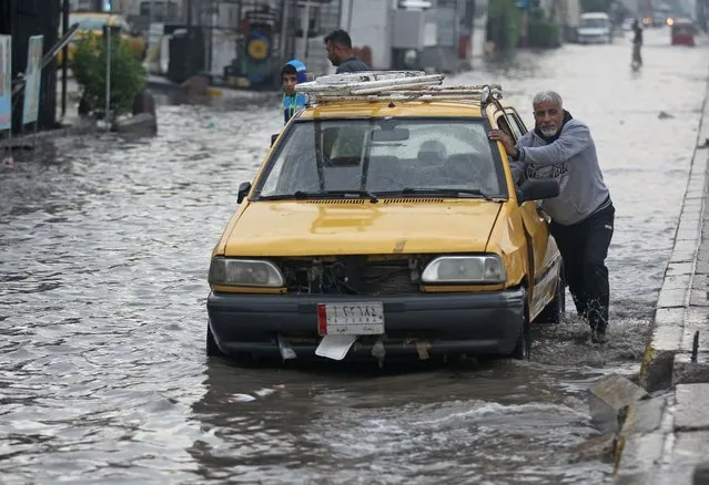 A driver pushes his vehicle through a flooded street caused by rainfall in Sadr City, east of the Iraqi capital Baghdad, on November 21, 2020. (Photo by Ahmad Al-Rubaye/AFP Photo)