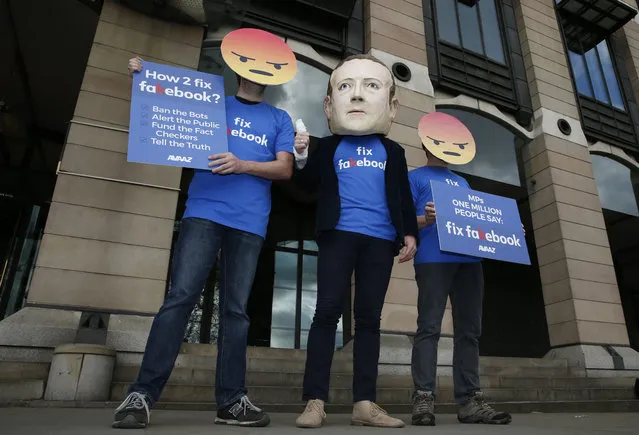 A protester wearing a mask with the face of Facebook founder Mark Zuckerberg, in between men wearing angry face emoji masks,  during a protest against Facebook outside Portcullis in London, Thursday, April 26, 2018, as the Chief Technical Officer of Facebook Mike Schroepfer is due to give evidence on the companies use of data from its customers in front of a Parliamentary Select Committee. (Photo by Alastair Grant/AP Photo)