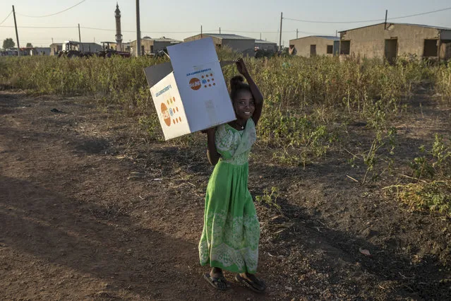 A Tigray refugee girl who fled a conflict in the Ethiopia's Tigray region, carries an empty UNFP distribution box at Village 8, the transit centre near the Lugdi border crossing, eastern Sudan, Sunday, November 22, 2020. (Photo by Nariman El-Mofty/AP Photo)