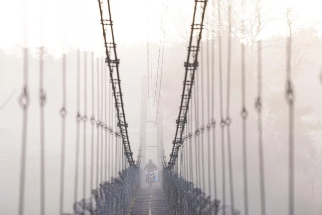 A man on a motorcycle crosses a suspension bridge over the Bagmati river in Lalitpur, Nepal, Monday, March 27, 2023. (Photo by Niranjan Shrestha/AP Photo)