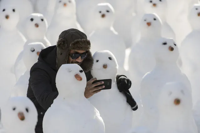 A man surrounded by snowmen takes a selfie with a cell phone during a protest against the Davos World Economic Forum, WEF, in Davos, Switzerland, Saturday, January 24, 2015. The world's financial and political forum at the Swiss ski resort will end today. (Photo by Jean-Christophe Bott/AP Photo/Keystone)