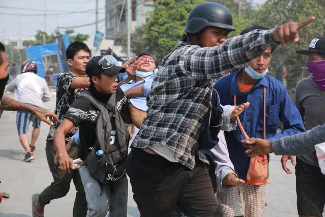 A man with a head injury is carried by other men Monday, March 22, 2021 in Mandalay, Myanmar. (Photo by AP Photo/Stringer)