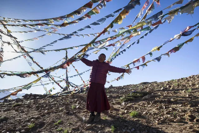 In this photograph taken on July 7, 2018, an Indian Buddhist monk plays with the wind amongst prayer flags on a hill overlooking Tnagyud Gompa monastery in Komik in Spiti Valley in the northern state of Himachal Pradesh. (Photo by Xavier Galiana/AFP Photo)