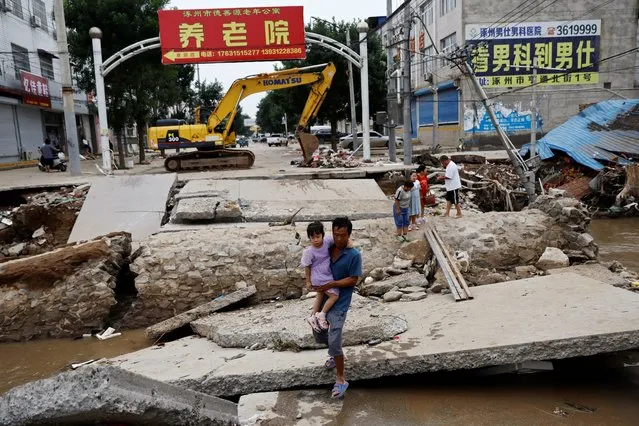 A man holding a child walks across a damaged bridge after the rains and floods brought by remnants of Typhoon Doksuri, in Zhuozhou, Hebei province, China on August 7, 2023. (Photo by Tingshu Wang/Reuters)