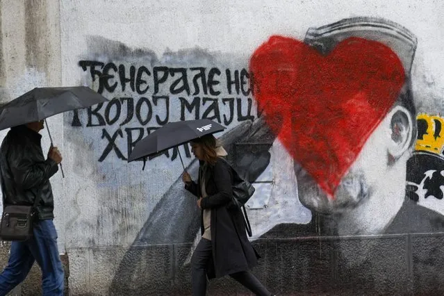 People walk by a mural of former Bosnian Serb military chief Ratko Mladic vandalized with red paint in Belgrade, Serbia, Monday, May 8, 2023. Mladic is serving a life sentence for genocide during the 1992-95 War in Bosnia but whom many Serbs still consider a hero. (Photo by Darko Vojinovic/AP Photo)