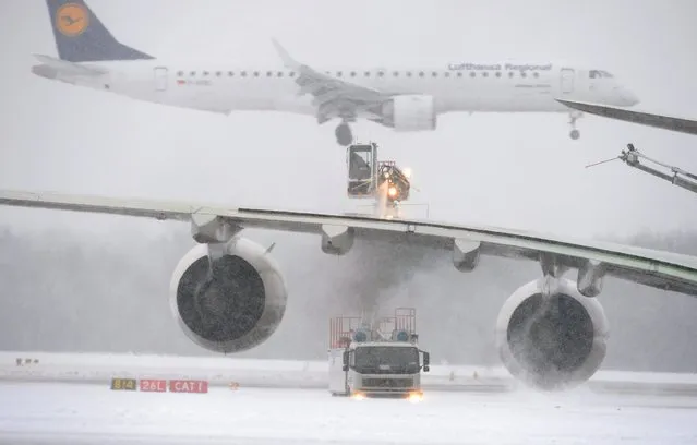 An airplane is cleared of snow and ice, while an airplane lands in the background at the snowcapped airport in Munich, Germany, 30 December 2014. 45 take-offs and landings were cancelled due to weather conditions so far. (Photo by Andreas Gebert/EPA)