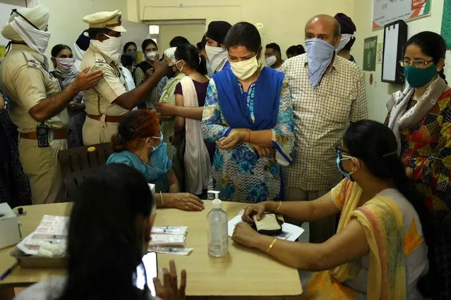 Police personnel gesture to people waiting for their turn to receive a dose of the Covid-19 coronavirus vaccine at a health centre in Amritsar on May 10, 2021. (Photo by Narinder Nanu/AFP Photo)