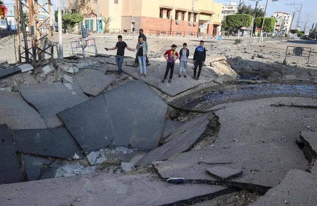 Palestinian youths take pictures with their smart phones of a huge crater on a main road in Gaza City on May 13, 2021 following continued Israeli airstrikes overnight on the Hamas-controlled Gaza Strip. The Israeli army has launched hundreds of air strikes on the Gaza Strip since the begining of the week, while Palestinian militants have launched more than 1,200 rockets, according to Israel's army, in some of the worst violence in seven years in the area. (Photo by Mahmud Hams/AFP Photo)