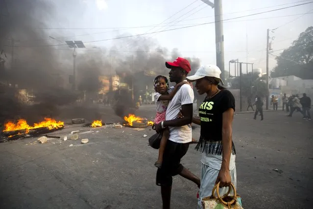 People walk past a barricade during a protest over the cost of fuel in Port-au-Prince, Haiti, Friday, July 6, 2018. Major protests erupted Friday in Haiti as the government announced a sharp increase in gasoline prices, with demonstrators using burning tires and barricades to block major streets across the capital and in the northern city of Cap-Haitien. (Photo by Dieu Nalio Chery/AP Photo)