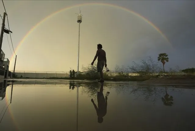 A construction worker walks for catching fish as a rainbow appears over Sre Ampel village on the outskirts of Phnom Penh, Cambodia, Monday, June 19, 2023. (Photo by Heng Sinith/AP Photo)
