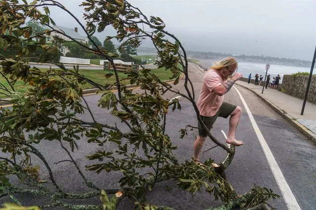 Zeke Baker steps over a fallen tree branch while clearing debris from a sidewalk as Tropical Storm Henri moves through the area in Newport, R.I., Sunday, August 22, 2021. (Photo by David Goldman/AP Photo)