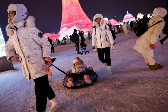 A visitor pulls a tire with a child sitting on it at the Harbin International Ice and Snow Festival, in Harbin, Heilongjiang province, China on January 4, 2024. (Photo by Tingshu Wang/Reuters)