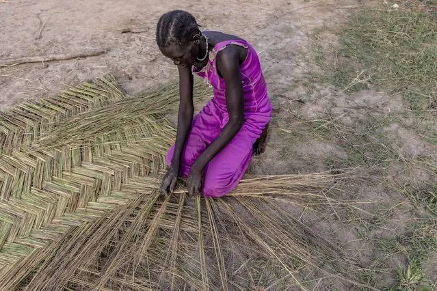 Abuk Yel, 28, makes “audek”, a braided dry grass that will serve to build herself a shelter, in Langic, Northern Bahr el Ghazal State, South Sudan, Wednesday, October 20, 2021. Yel, who was forced out of her home by the floods earlier in the month, builds a shelter to live in with her six children. (Photo by Adrienne Surprenant/AP Photo)