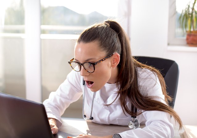 Young woman doctor looking at laptop. Facial expression of shock. (Photo by Jevtic/Getty Images)