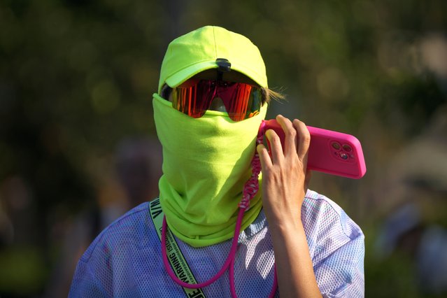 A man wearing a face cover uses his mobile phone as he walks during an unseasonably hot day in Beijing, Sunday, June 16, 2024. (Photo by Andy Wong/AP Photo)