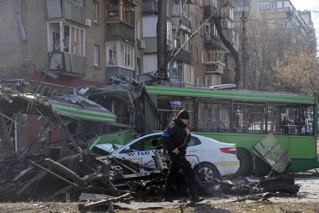 A Ukrainian soldier passes by a destroyed a trolleybus and taxi after a Russian bombing attack in Kyiv, Ukraine, Monday, March 14, 2022. (Photo by Efrem Lukatsky/AP Photo)