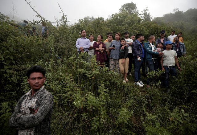 People watch as security force personnel prepare to carry the bodies of the victims at the site of a helicopter crash on the outskirts of Kathmandu, Nepal on August 7, 2024. (Photo by Navesh Chitrakar/Reuters)