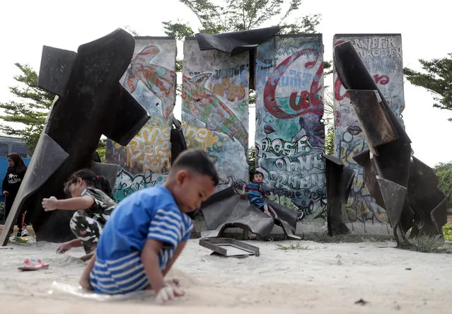 In this photo taken Sunday, August 4, 2019 Indonesian children play near pieces of Berlin Wall erected as parts of an installation art by Indonesian artist Teguh Ostenrik, at Kalijodo Park in Jakarta, Indonesia. For nearly three decades, the Berlin Wall encircled West Berlin, built by communist East German authorities ostensibly to protect the country from “fascists”, but in reality to prevent their own citizens from fleeing into the democratic half of the divided city, a portal to the rest of the free world. For a barrier meant to prevent travel, chips, chunks and full segments of the 156.4 kilometer-long (97.2 mile-long) reinforced concrete Wall have done a pretty good job themselves getting around Germany and the rest of the world in the past 30 years. (Photo by Dita Alangkara/AP Photo)