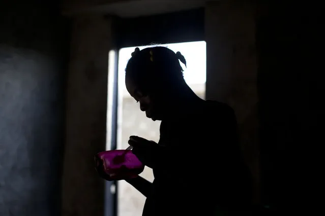 In this June 27, 2015 photo, Fritzna Oralist, 12, eats lunch inside an abandoned shipping depot where she lives with her mother and three brothers in Port-au-Prince, Haiti. After the 2010 earthquake, some residents returned to unsafe homes or moved into damaged and abandoned buildings across the capital. (Photo by Rebecca Blackwell/AP Photo)