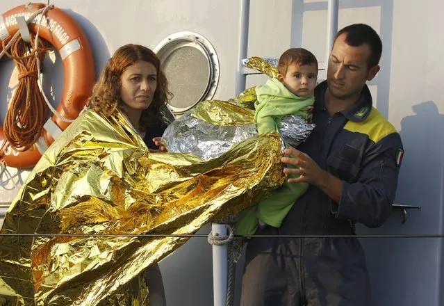 An Italian coast guard officer helps Syrian refugees from Kobani in the port of Kos following a rescue mission off the Greek island of Kos August 10, 2015. (Photo by Yannis Behrakis/Reuters)
