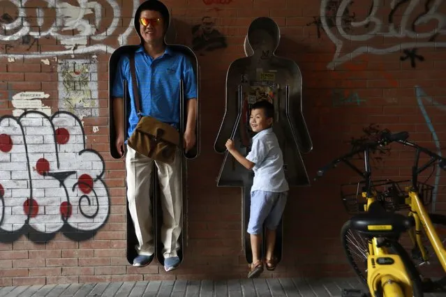 Visitors squeeze themselves into sculptures for pictures at 798 Art district in Beijing, China, 26 August 2017. The Beijing 798 art district is made up of a complex of decommissioned military factory buildings, housing a variety of quirky art galleries and cafes popular with tourists and young people. (Photo by How Hwee Young/EPA/EFE)