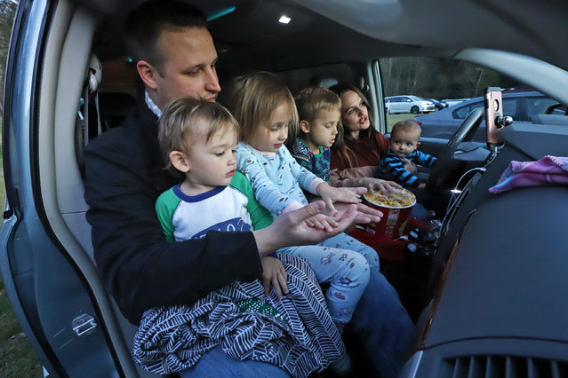 Pastor Marc Lickins, top left, of the Harvest Baptist Church in Harrison, Pa., gathers with his family, from left to right, Cruz, 2, Willow, 3, Evennan, 5, wife Maggie, and Deacon, 6 months, in the front of their minivan to watch the first screening of an Easter service, produced by the church, at the Riverside Drive-In theater in Park Township, Pa., at sunset Friday, April 10, 2020. The service will be screened each night through Easter Sunday. (Photo by Gene J. Puskar/AP Photo)
