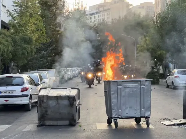 In this Tuesday, September 20, 2022, photo taken by an individual not employed by the Associated Press and obtained by the AP outside Iran, a trash bin is burning as anti-riot police arrive during a protest over the death of a young woman who had been detained for violating the country's conservative dress code, in downtown Tehran, Iran. Iran faced international criticism on Tuesday over the death of a woman held by its morality police, which ignited three days of protests, including clashes with security forces in the capital and other unrest that claimed at least three lives. (Photo by AP Photo/Stringer)