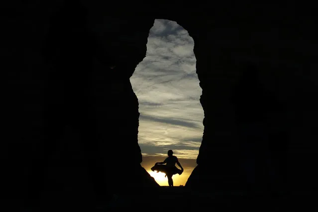 A woman traveling with a group of friends driving from Florida to Colorado is silhouetted against the setting sun as the group visits Monument Rocks, Wednesday, May 20, 2020, south of Oakley, Kan. As states slowly lift restrictions meant to stem the spread of COVID-19, people are beginning to hit the road after spending months in their homes. (Photo by Charlie Riedel/AP Photo)