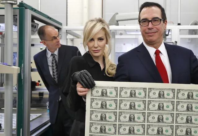 Treasury Secretary Steven Mnuchin, right, and his wife Louise Linton, hold up a sheet of new $1 bills, the first currency notes bearing his and U.S. Treasurer Jovita Carranza's signatures, Wednesday, November 15, 2017, at the Bureau of Engraving and Printing (BEP) in Washington. The Mnuchin-Carranza notes, which are a new series of 2017, 50-subject $1 notes, will be sent to the Federal Reserve to issue into circulation. At left is BEP Director Leonard Olijar. (Photo by Jacquelyn Martin/AP Photo)