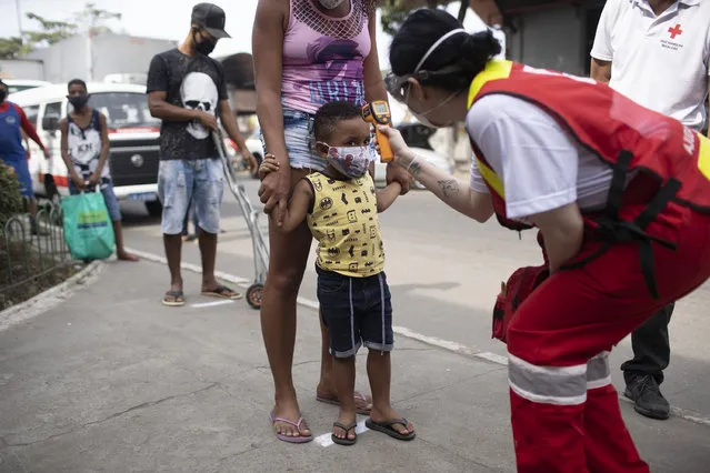 A member of the Red Cross checks the temperature of a child at the CEASA, Rio de Janeiro's main wholesale market, amid the new coronavirus pandemic in Rio de Janeiro, Brazil, Tuesday, June 23, 2020. (Photo by Silvia Izquierdo/AP Photo)