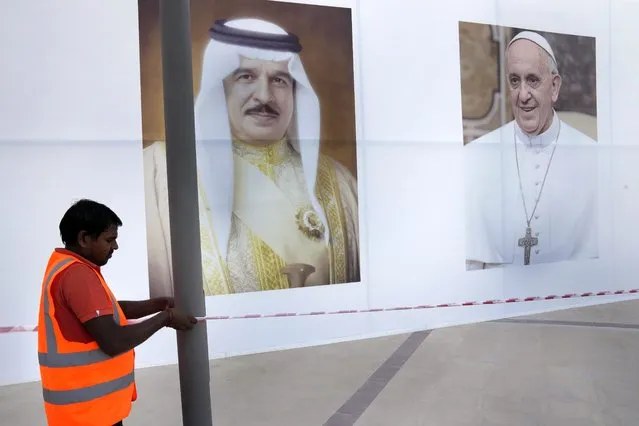 A worker hang a bar in front of portraits that show Pope Francis, right and Bahrain's King Hamad bin Isa Al Khalifa, left, outside the Cathedral of Our Lady of Arabia where the Pope will attend a Mass, in Manama, Bahrain, Wednesday, November 2, 2022. Pope Francis is making the November 3-6 visit to participate in a government-sponsored conference on East-West dialogue and to minister to Bahrain's tiny Catholic community, part of his effort to pursue dialogue with the Muslim world. (Photo by Hussein Malla/AP Photo)