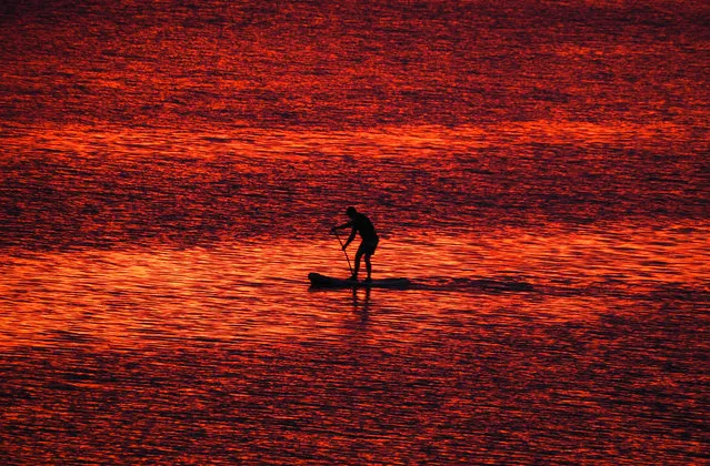 A man steers his stand-up paddle board at sunset on the Velikaya River in Pskov, 300km (187 miles) South-West from St.Petersburg, Russia, Monday, July 6, 2020. (Photo by Dmitri Lovetsky/AP Photo)