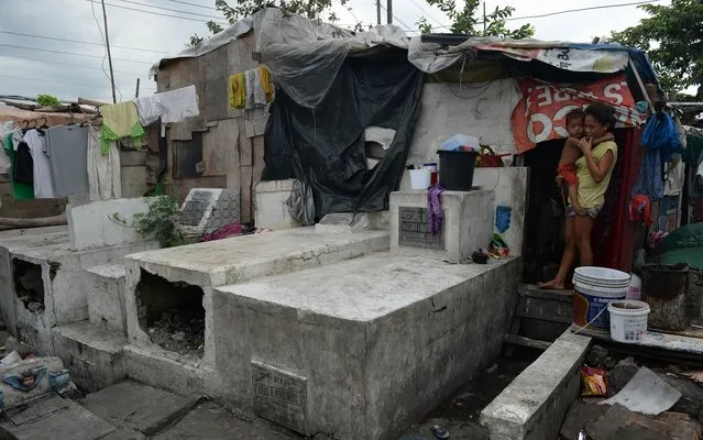 A mother carries her child at the entrance of their house buillt next to the tombs at a cemetery in Manila on October 31, 2014, days ahead of the traditional All Souls' day. Millions across the Philippines will visit cemeteries to pay their respects to their dead, in an annual tradition that combines catholic religious rites with the country's penchant for festivity. (Photo by Ted Aljibe/AFP Photo)