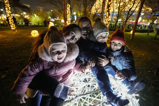 Children pose on a light installation at a Christmas fair which opened ahead of the holiday season in Bucharest, Romania, Friday, November 25, 2022. Municipal authorities in the Romanian capital, quoted by local media, stated that holiday season city light decoration levels will remain at last year's level and use energy saving solutions. (Photo by Andreea Alexandru/AP Photo)