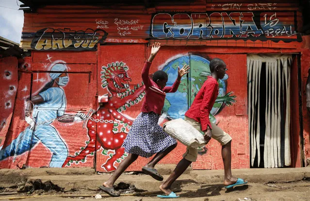 In this June 3, 2020, file photo, children run down a street past an informational mural warning people about the dangers of the new coronavirus, in the Kibera slum, or informal settlement, of Nairobi, Kenya. A new snapshot of the frantic global response to the coronavirus pandemic shows some of the world's largest government donors of humanitarian assistance are buckling under the strain and overall aid commitments have dropped by a third from the same period last year. (Photo by Brian Inganga/AP Photo/File)
