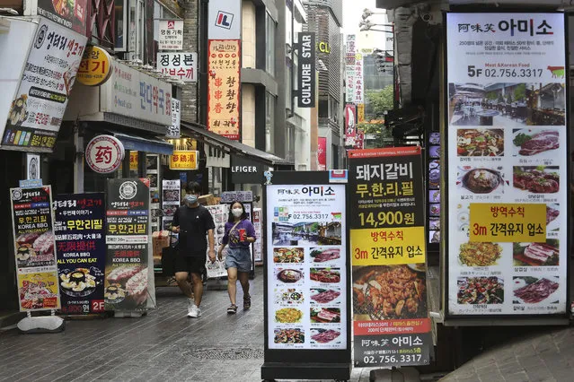 People wearing face masks to help protect against the spread of the coronavirus pass by banners showing the menu items of restaurants in Seoul, South Korea, Friday, August 28, 2020. South Korean officials are considering reducing working hours of restaurants and cafes as the country counted its 15th straight day of triple-digit jumps in coronavirus infections. (Photo by Ahn Young-joon/AP Photo)