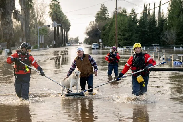 San Diego firefighters help Humberto Maciel rescue his dog  from his flooded home in Merced, California, on January 10, 2023. Relentless storms were ravaging California again Tuesday, the latest bout of extreme weather that has left 14 people dead. Fierce storms caused flash flooding, closed key highways, toppled trees and swept away drivers and passengers – reportedly including a five-year-old-boy who remains missing in central California. (Photo by Josh Edelson/AFP Photo)