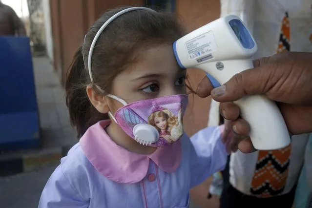 A worker checks the body temperature of a student on her arrival at a primary school in Lahore, Pakistan, Wednesday, September 30, 2020. Pakistani students head back to primary schools following their reopening, amid a steady decline in coronavirus deaths and infections. (Photo by K.M. Chaudary/AP Photo)