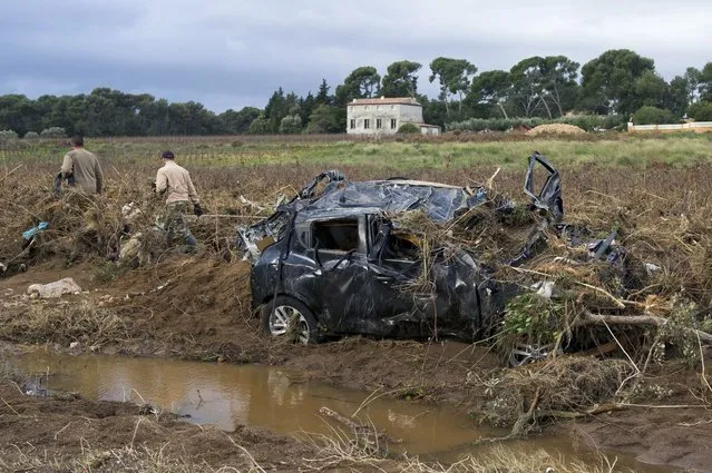 People walk next to a wrecked car near a river on November 28, 2014 in La Londe-les-Maures, southeastern France, after a violent storm which caused floods, damages and three deaths. The car is believed to have belonged to one of the victims. Three people are reported to have died in storms which have hit southeast France, and two are still reported missing. (Photo by Bertrand Langlois/AFP Photo)